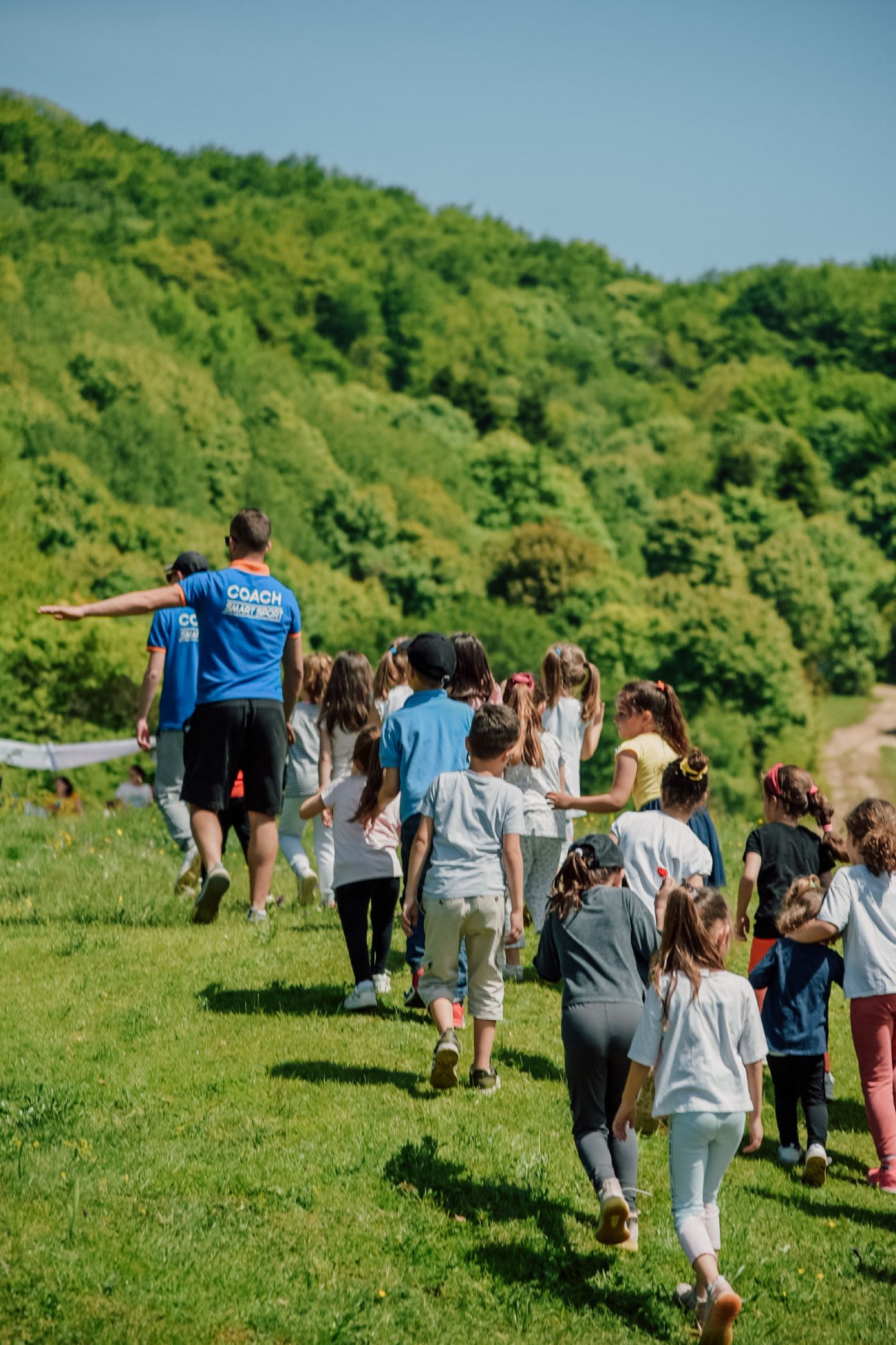 An adult leads children across a grassy hillside on a field trip