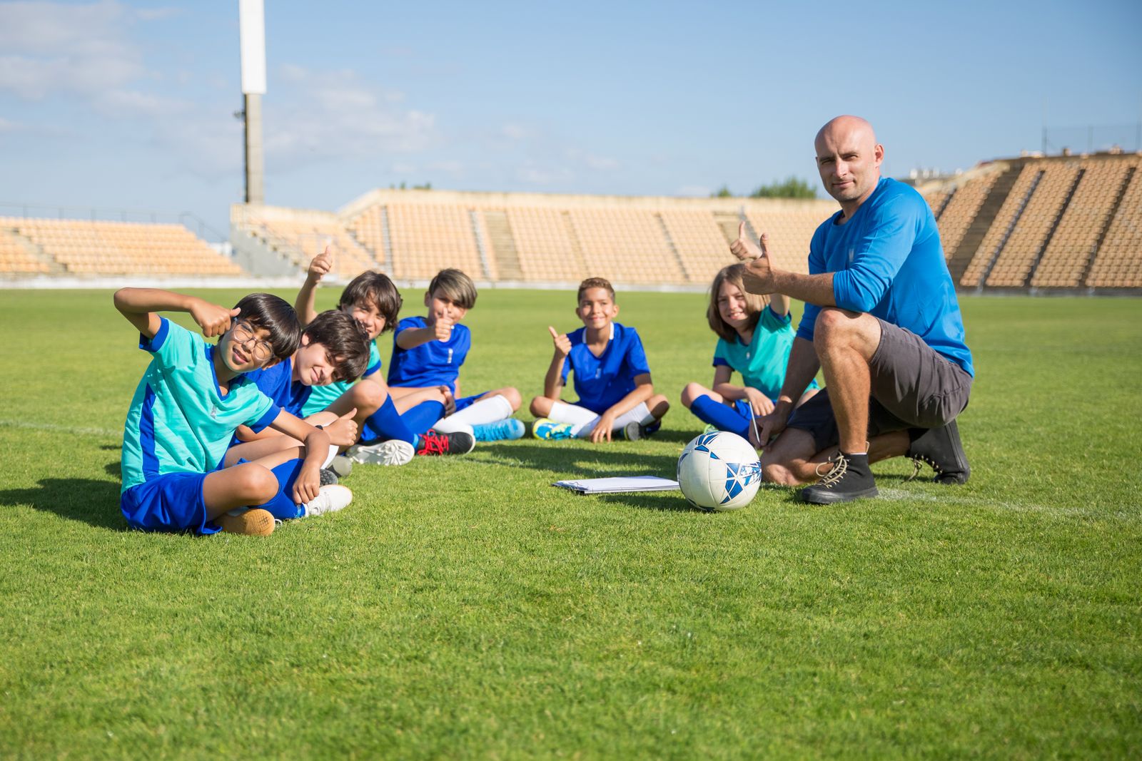 A coach sitting with young soccer players on the field